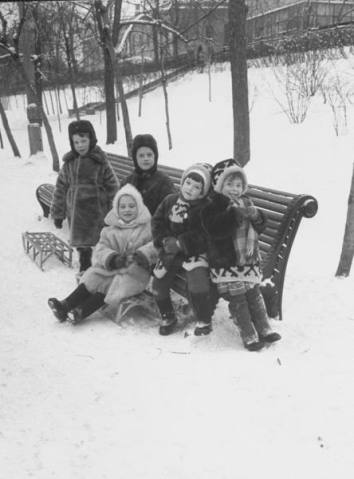 Children bundled up against the cold winter weather taking a break on a bench from sleighing