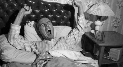 1950s yawning stretching man waking up in bed with tufted leather headboard